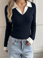 A woman wearing a navy blue cable-knit V-neck sweater with a contrasting white collar and white ribbed cuffs, paired with light-wash jeans.