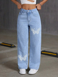 Person wearing light blue jeans with butterfly designs on a gray background