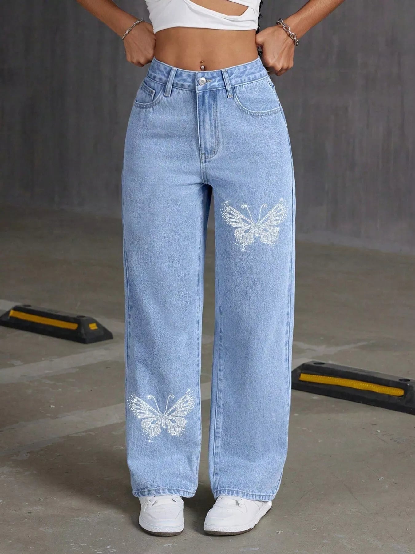 Person wearing light blue jeans with butterfly designs on a gray background