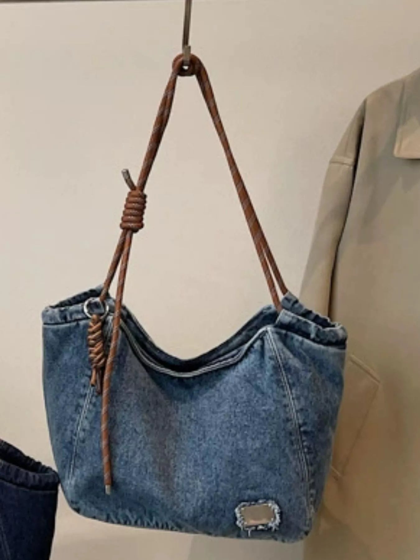 Blue denim handbag with brown leather handle hanging on a hook.