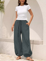 Woman wearing a white t-shirt and gray wide-leg pants standing against a light-colored wall.