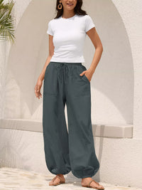 Woman wearing a white t-shirt and gray wide-leg pants standing against a light-colored wall.
