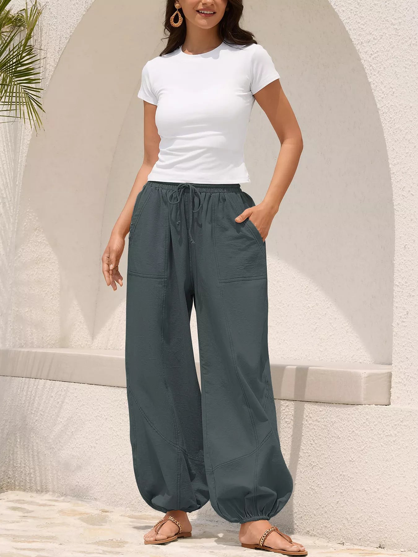 Woman wearing a white t-shirt and gray wide-leg pants standing against a light-colored wall.