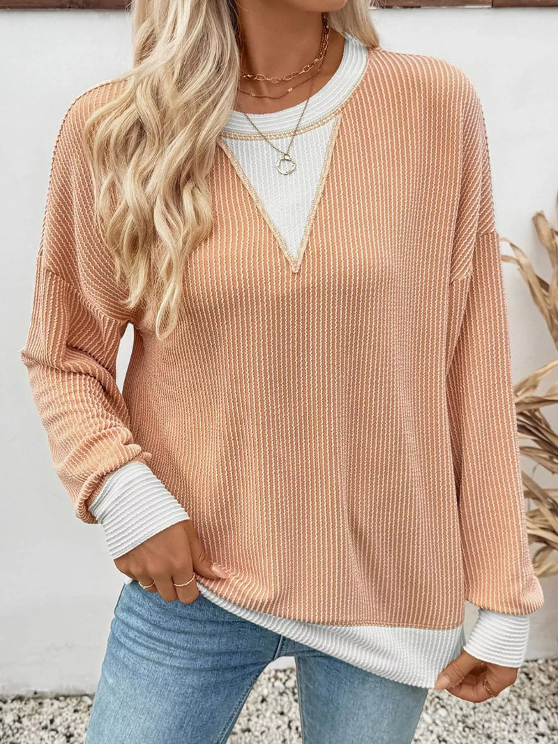 Person wearing a ribbed beige sweater over a white shirt with blue jeans against a neutral background