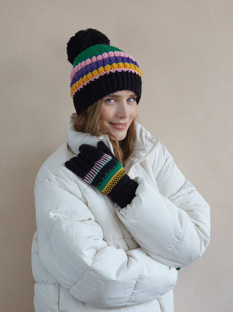 A woman wearing a black winter coat and touchscreen-compatible gloves with a striped pattern.