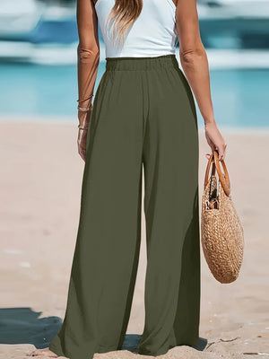 Person wearing green wide-leg pants and a white top on a beach.