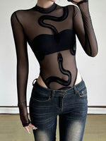Person wearing a black sheer top with snake design and high-waisted black pants on a dark background