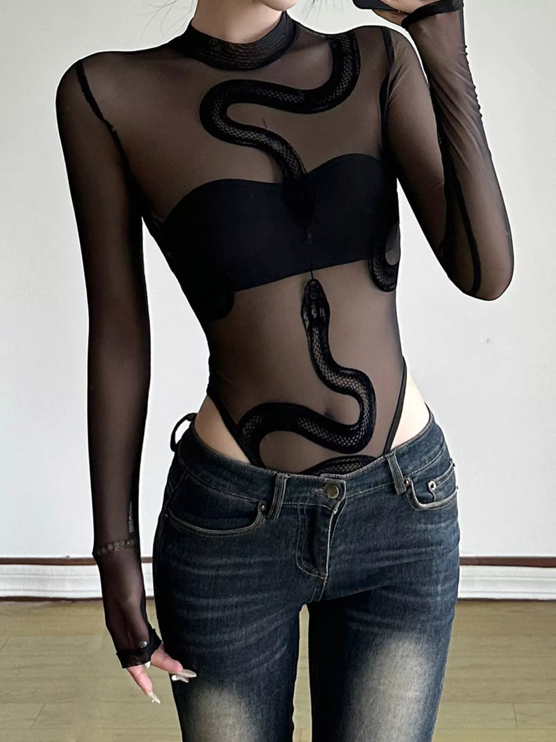 Person wearing a black sheer top with snake design and high-waisted black pants on a dark background
