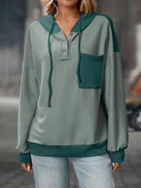 Green sweater with a hood and pocket worn by a person, blurred background