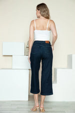Woman wearing a white top and dark blue jeans standing in a minimalistic room.