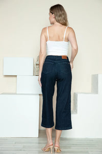 Woman wearing a white top and dark blue jeans standing in a minimalistic room.