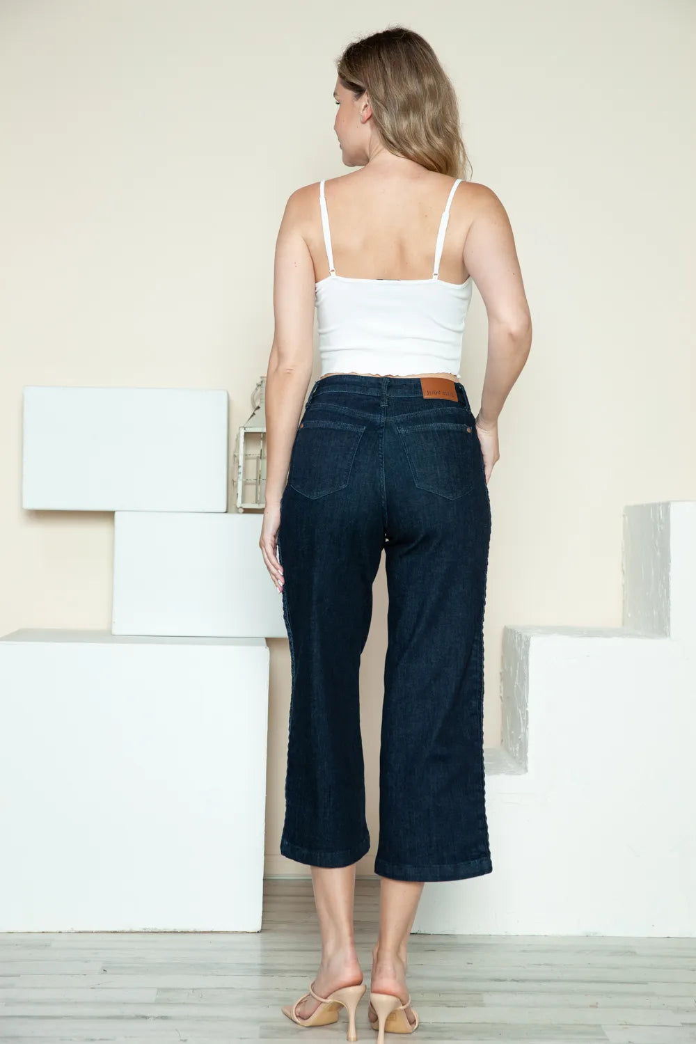 Woman wearing a white top and dark blue jeans standing in a minimalistic room.