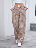 Person wearing brown checkered pants standing on a stone pavement.