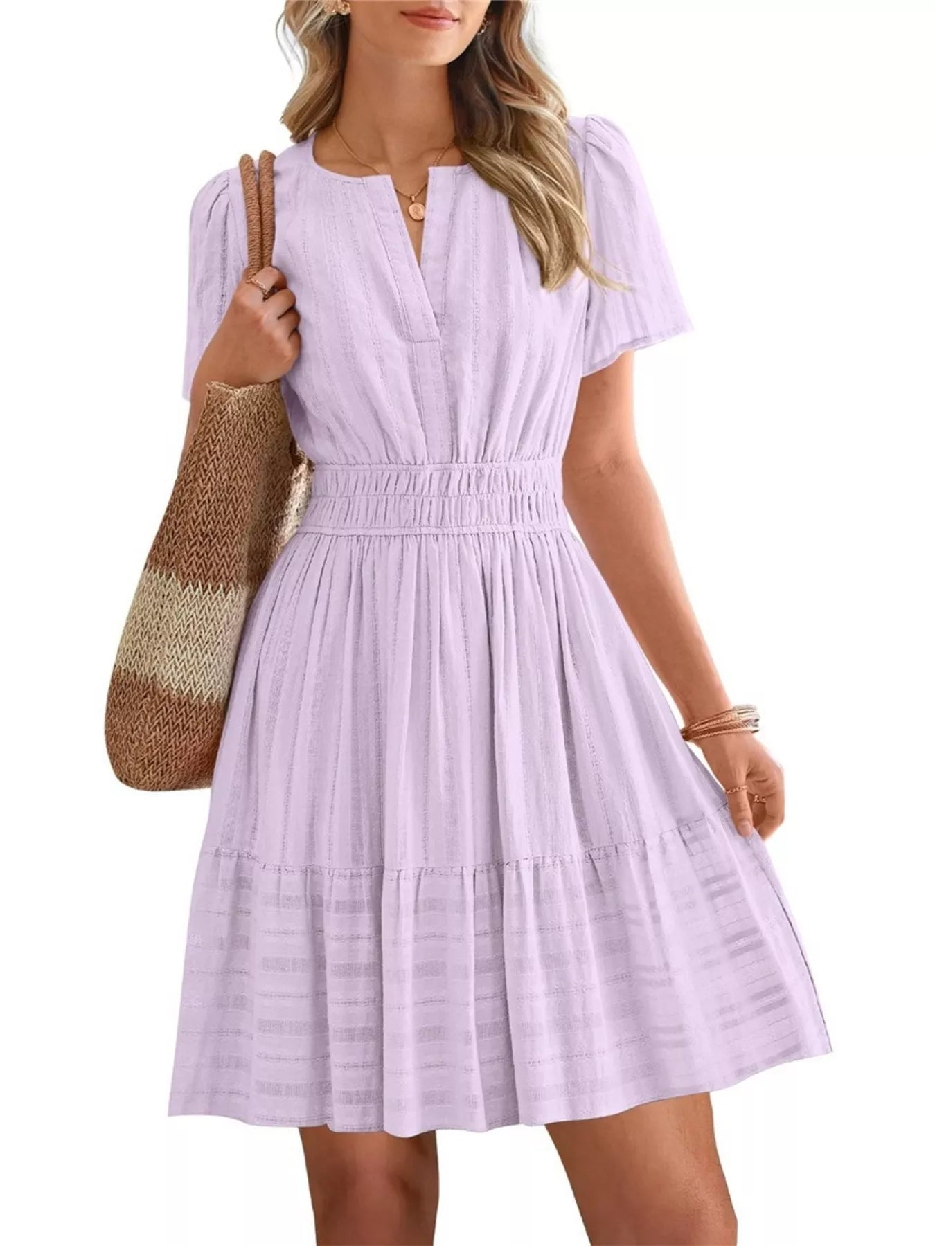 Woman wearing a light purple dress holding a brown bag on a white background