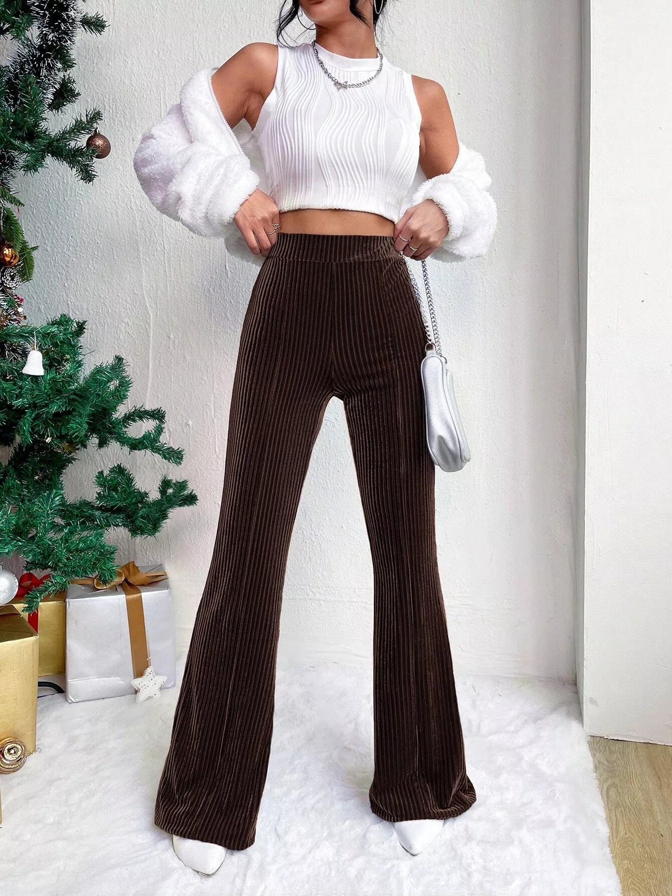 Person wearing a white top and brown ribbed pants in a minimalistic room with a Christmas tree.