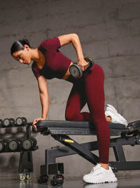 Woman exercising with dumbbells on a weight bench against a gray wall.