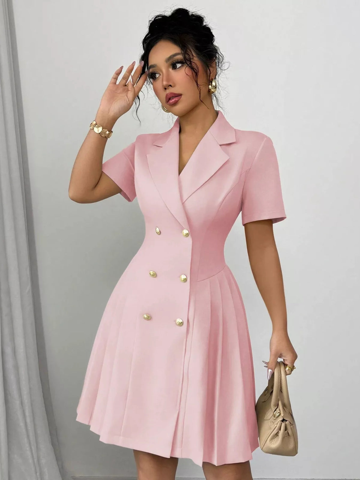 Woman wearing a pink dress with gold buttons against a gray background