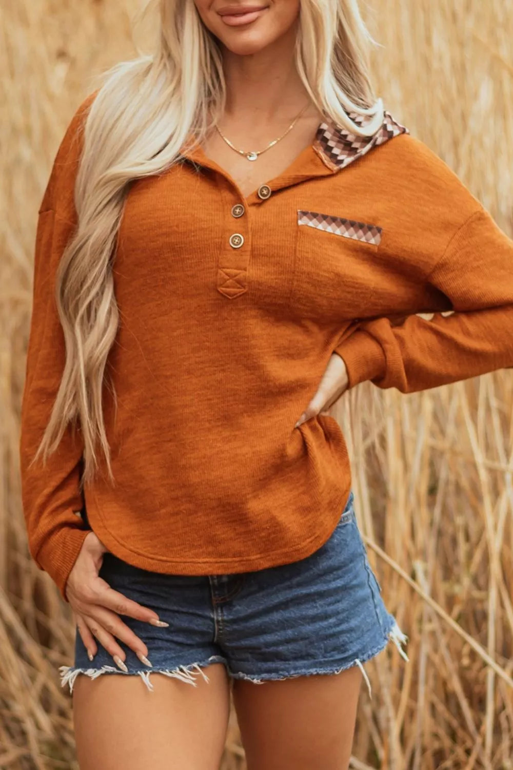 Woman wearing a rust-colored long-sleeve shirt with plaid accents in a field.