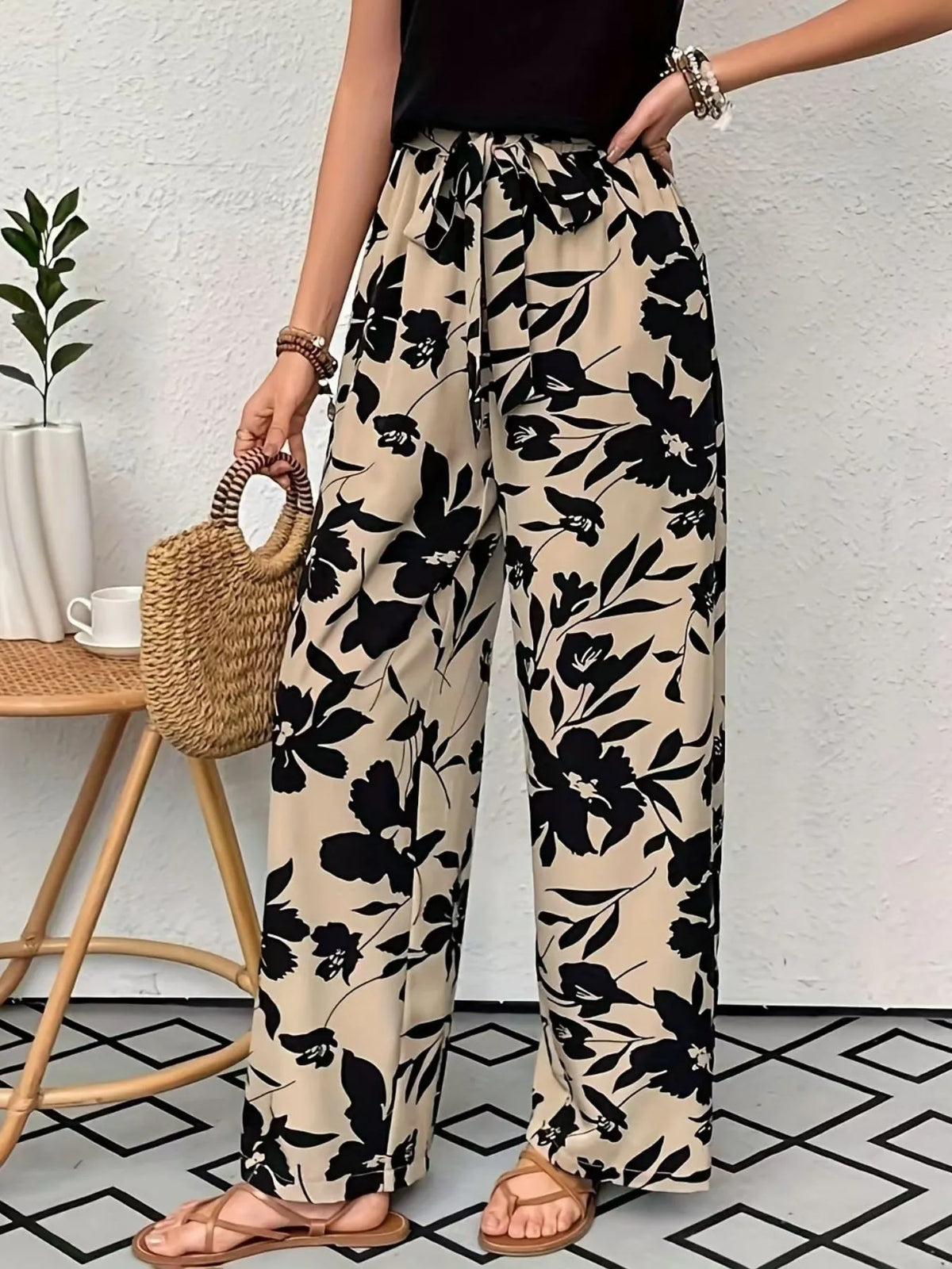 Person wearing black floral pants with a white wall and plant in the background