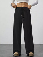 Person wearing black wide-leg pants with a white top on a plain background