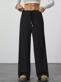 Person wearing black wide-leg pants with a white top on a plain background