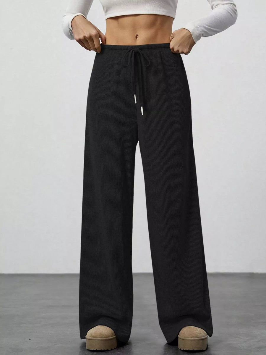Person wearing black wide-leg pants with a white top on a plain background