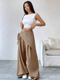 Woman wearing a white top and beige wide-leg pants in a minimalistic room.