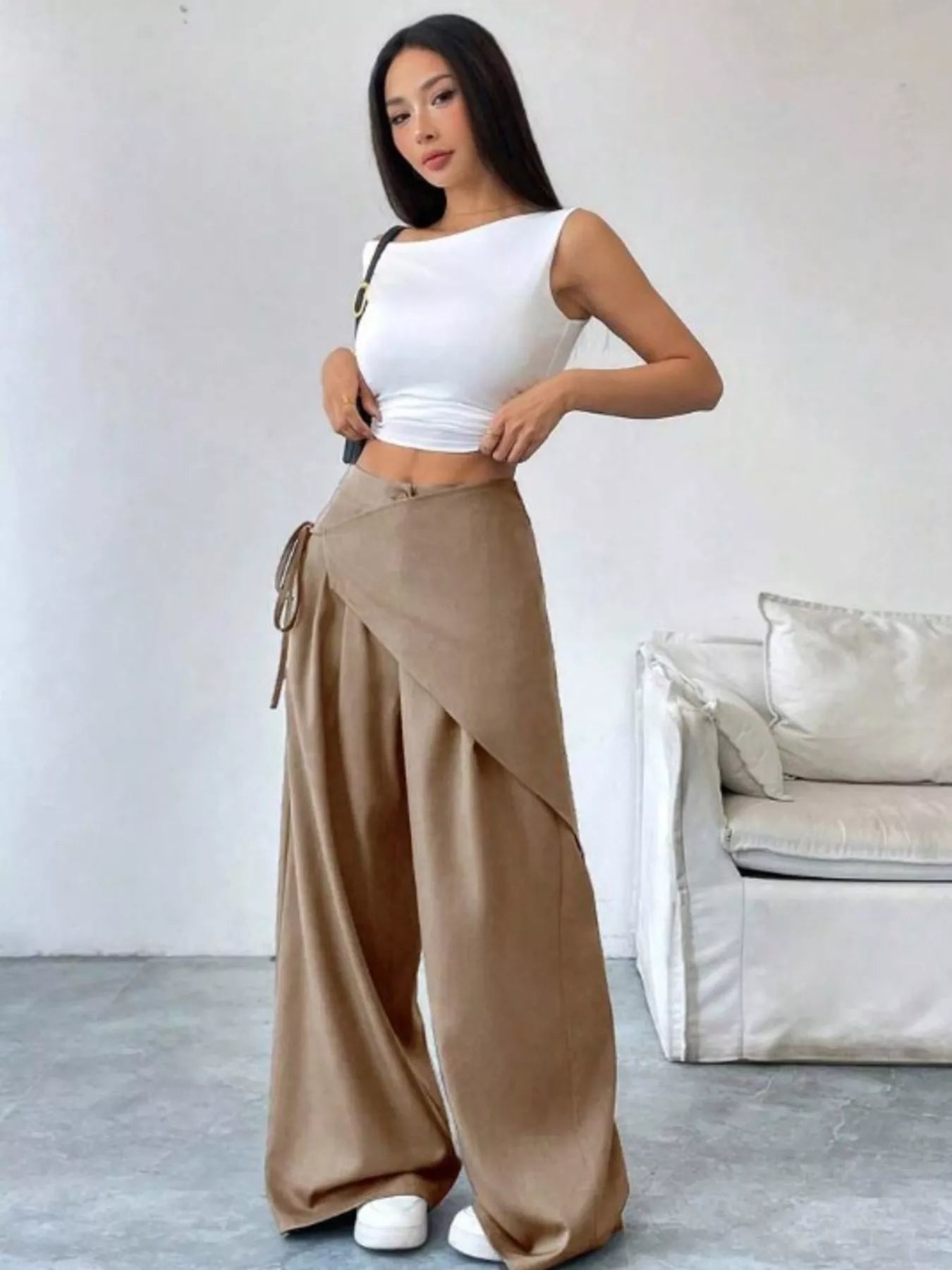 Woman wearing a white top and beige wide-leg pants in a minimalistic room.