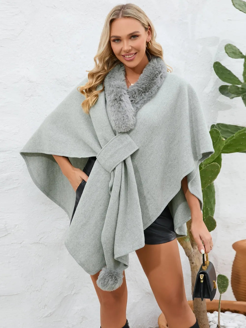 Woman wearing a gray poncho with fur trim against a white background