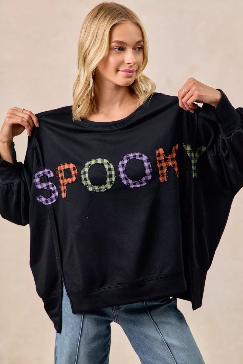 Woman wearing a black sweater with 'SPooky' in colorful letters, holding it up.