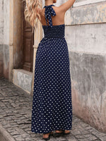 Woman wearing a navy blue polka dot dress standing against a stone wall.