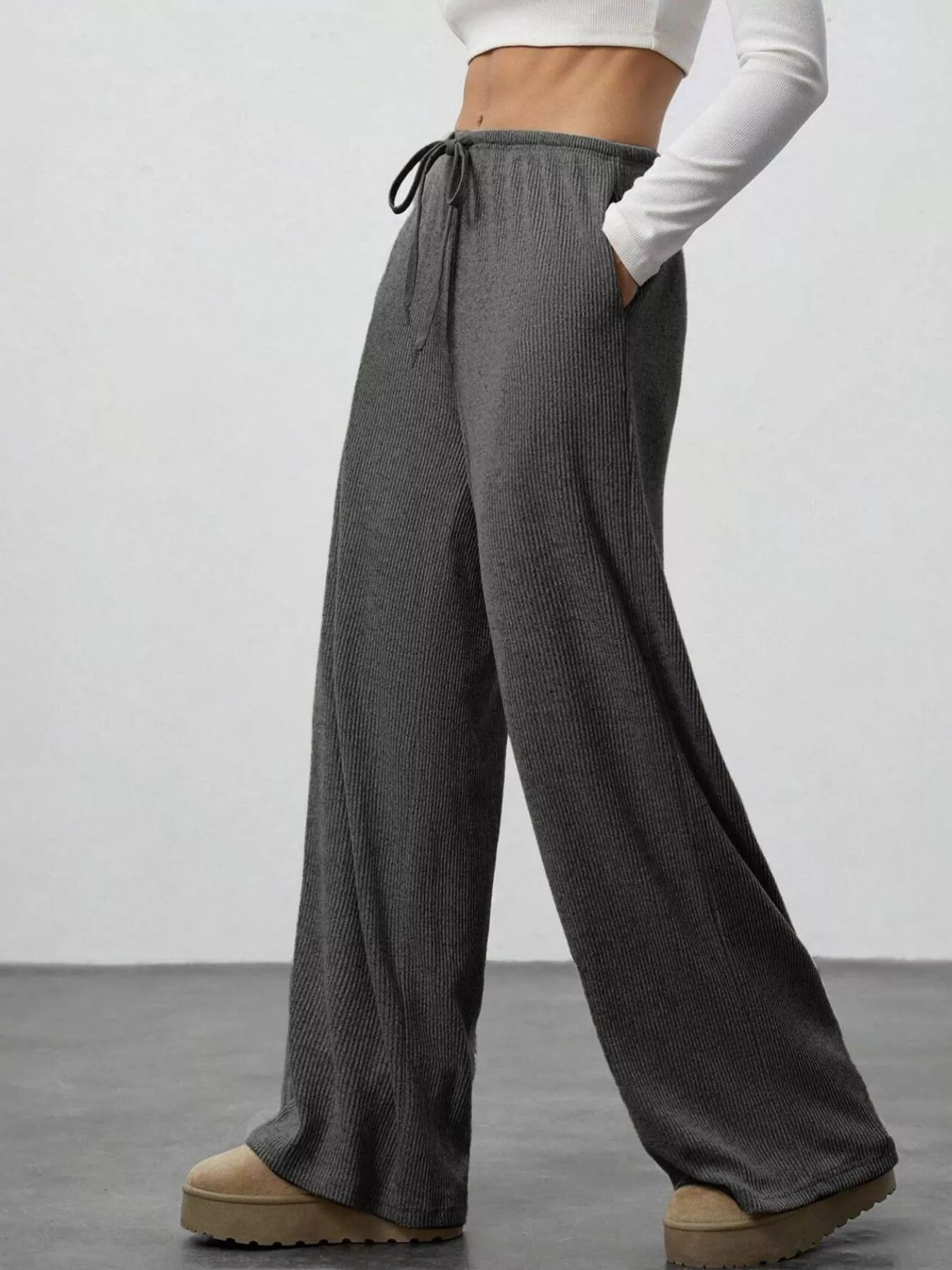 Person wearing gray wide-leg pants with a white top on a plain background