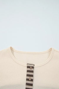 Close-up of a beige garment with a striped button on a light blue background