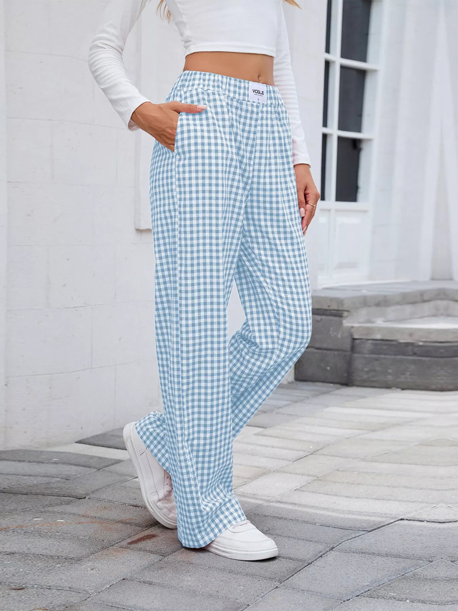 Person wearing light blue checkered pants and white sneakers on a stone pavement.