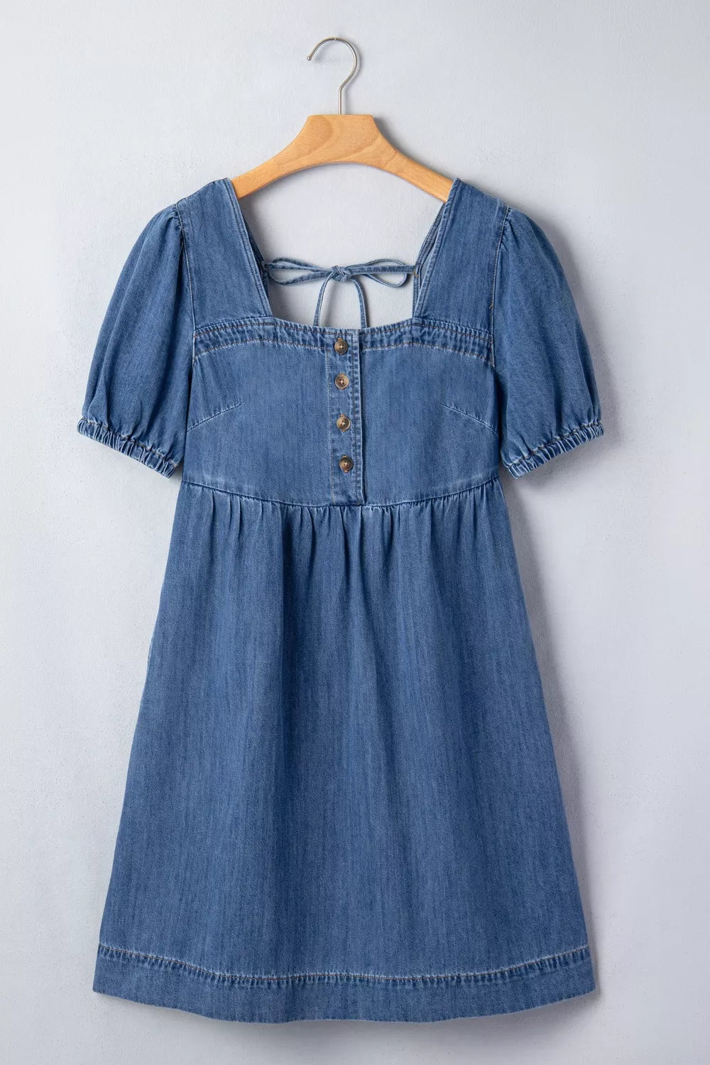 Blue denim dress on a wooden hanger against a white background