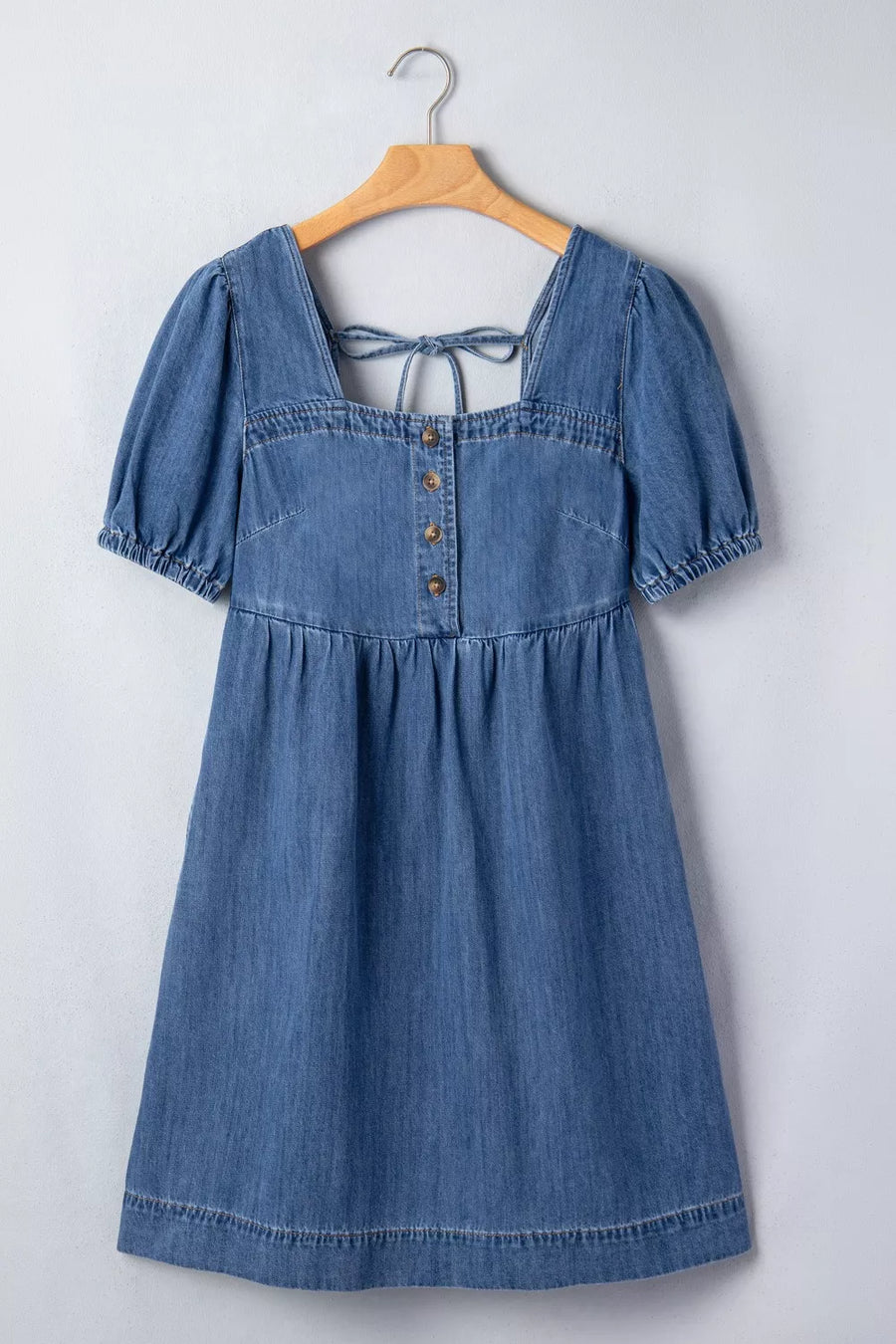 Blue denim dress on a wooden hanger against a white background