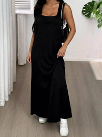 Person wearing a black sleeveless dress with white sneakers indoors.