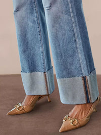 Cuffed blue jeans with beige high-heeled shoes on a brown background