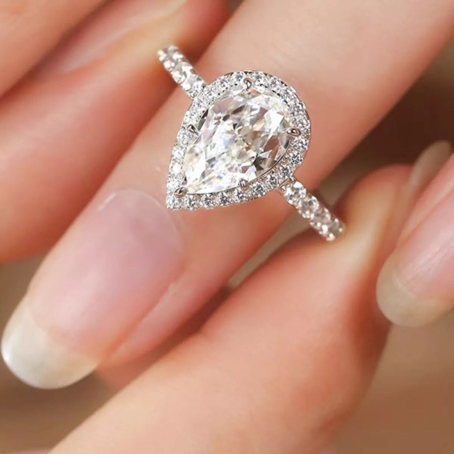 Diamond ring held between fingers with a soft focus background