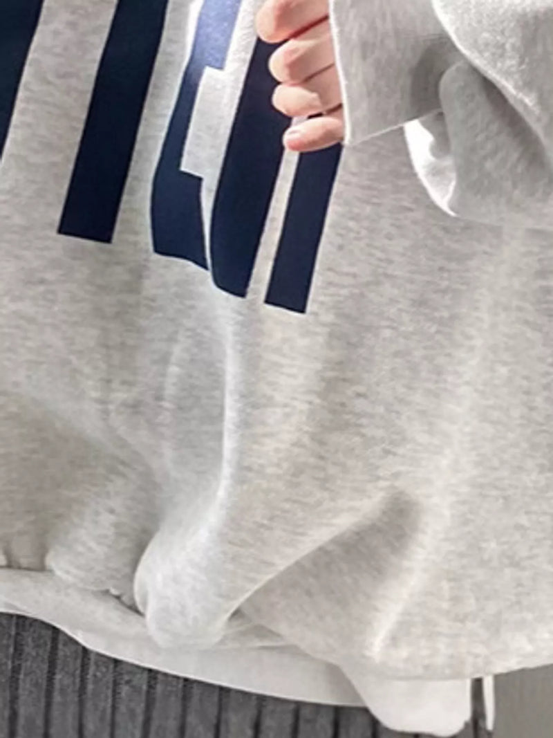 Close-up of a light heather gray sweatshirt with a large navy blue graphic print, worn by a person whose hand is visible near the collar.