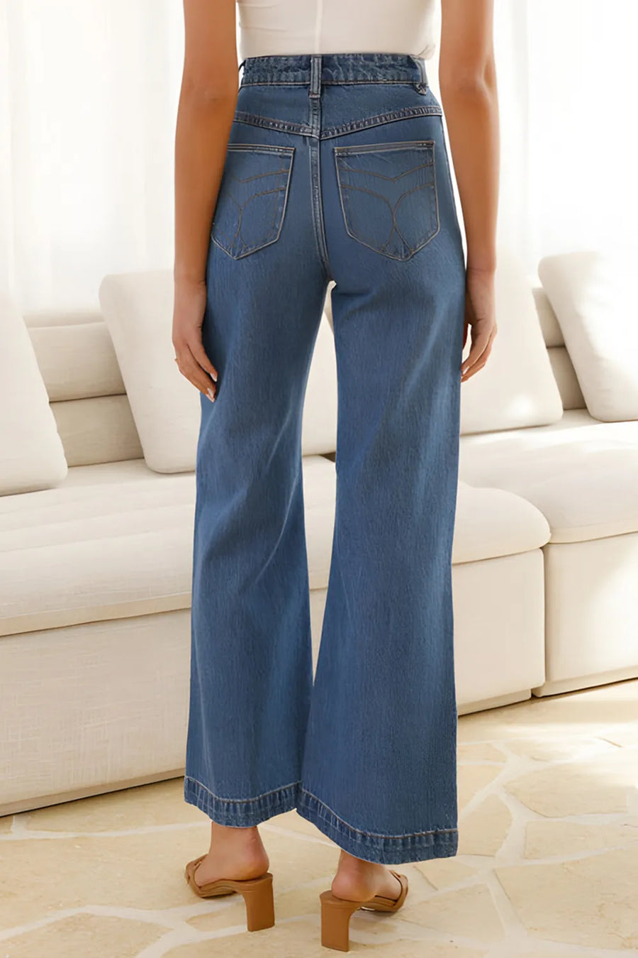 Person wearing blue jeans standing in a room with a white couch.