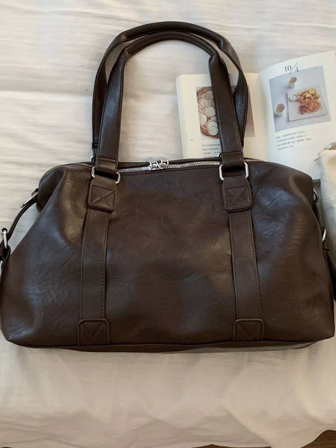 Brown leather duffel bag on a white surface with a magazine underneath