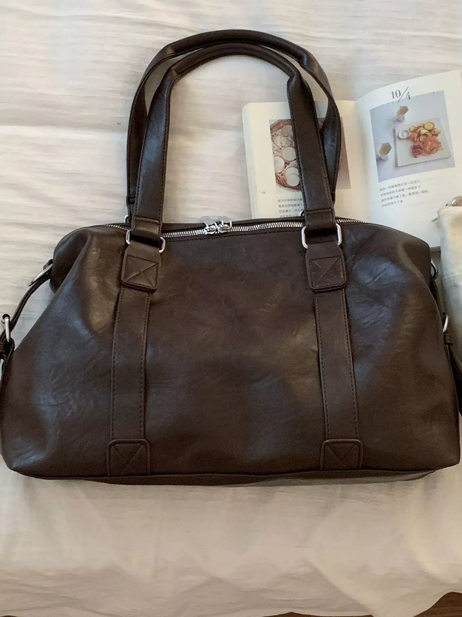 Brown leather duffel bag on a white surface with a magazine underneath