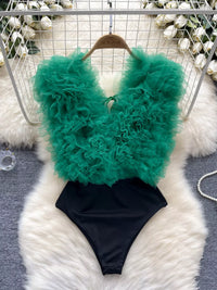 Green feathered top and black bottom swimsuit on a fluffy white surface.