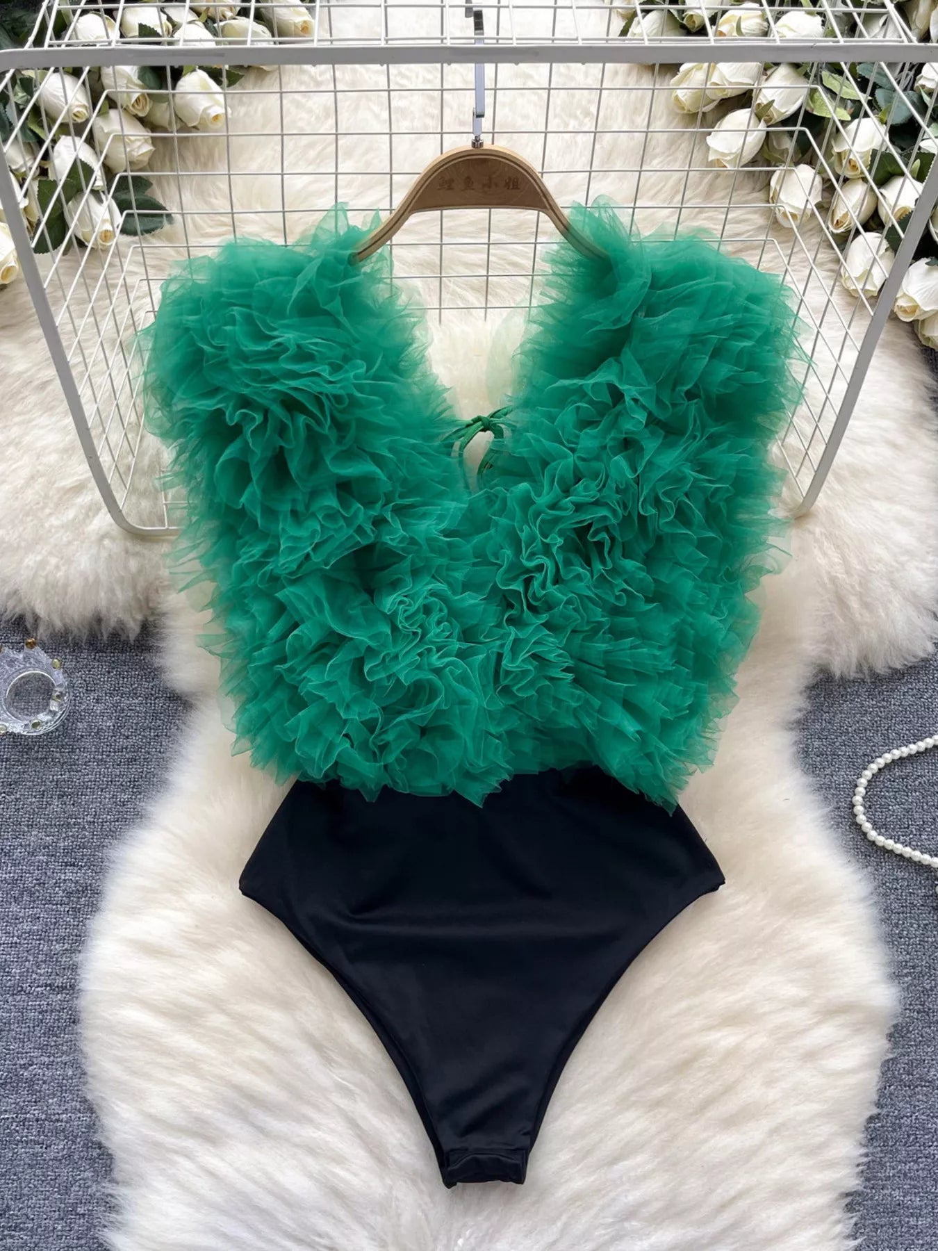 Green feathered top and black bottom swimsuit on a fluffy white surface.