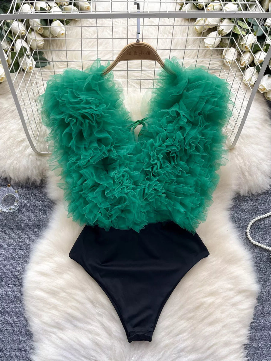Green feathered top and black bottom swimsuit on a fluffy white surface.