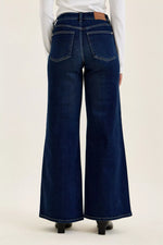 Dark blue flared jeans worn by a person on a white background