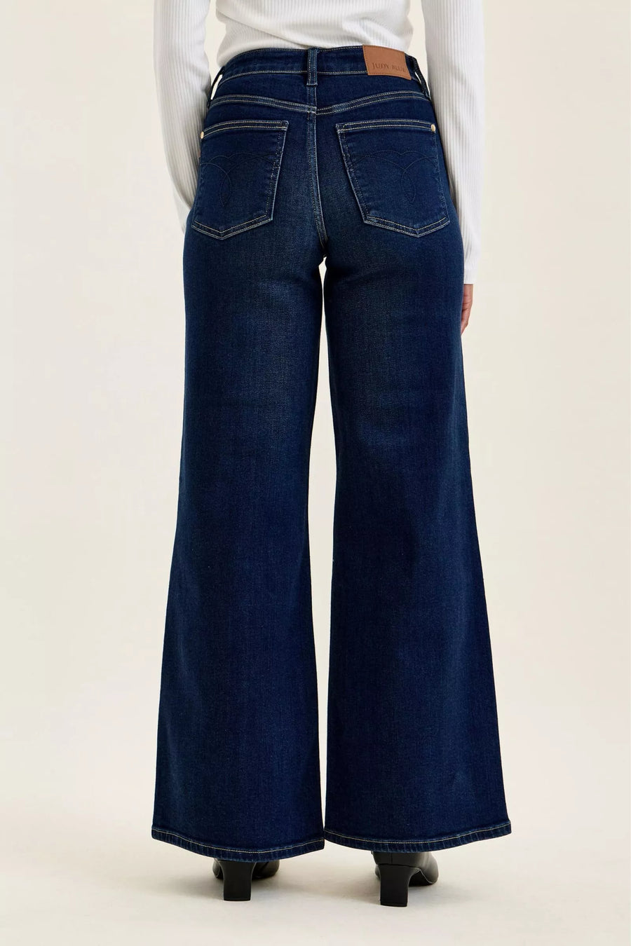 Dark blue flared jeans worn by a person on a white background