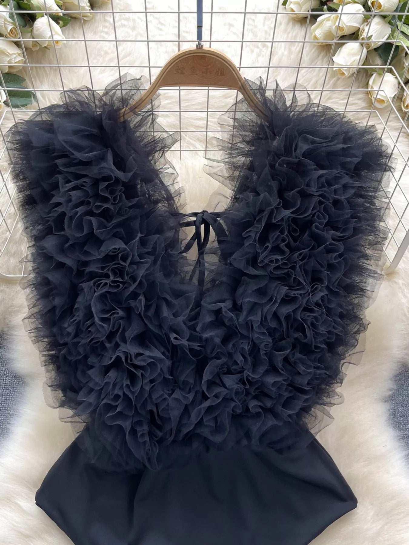 Black ruffled garment on a hanger against a floral background