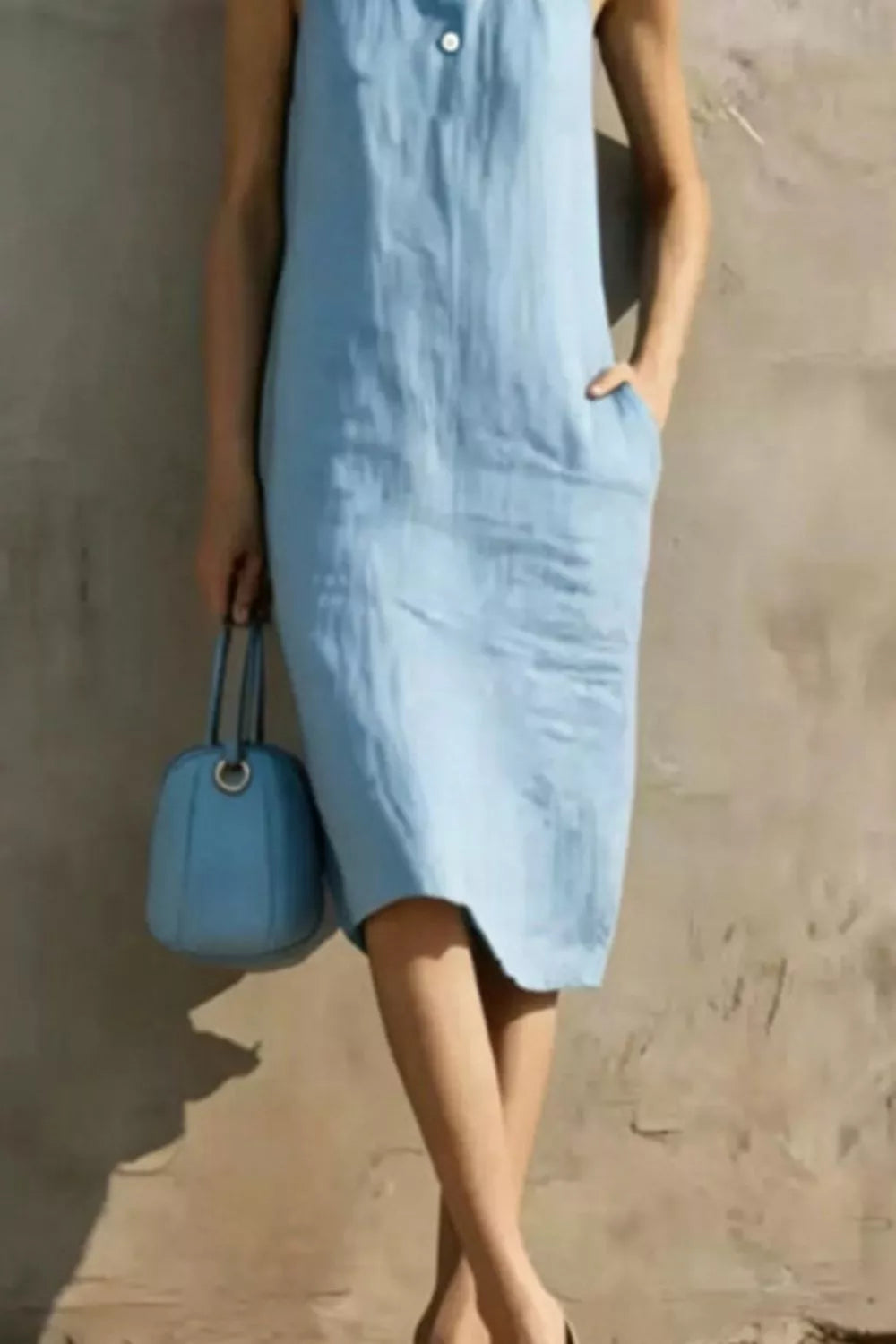 Person wearing a light blue dress holding a matching blue handbag against a neutral background